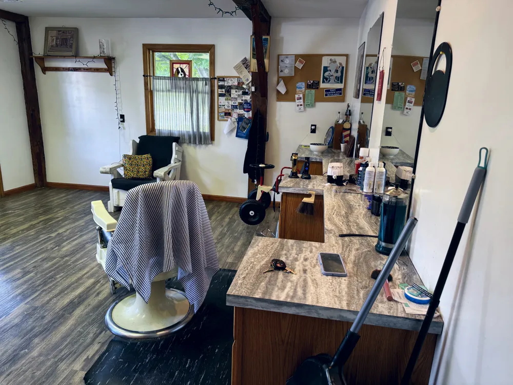 The antique barber chair draped with its striped cutting cape, mirrors and tools behind.
